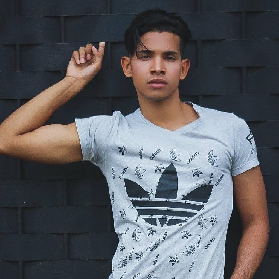 Joel Orasma Martinez — full-length portrait in Adidas tee against dark wall